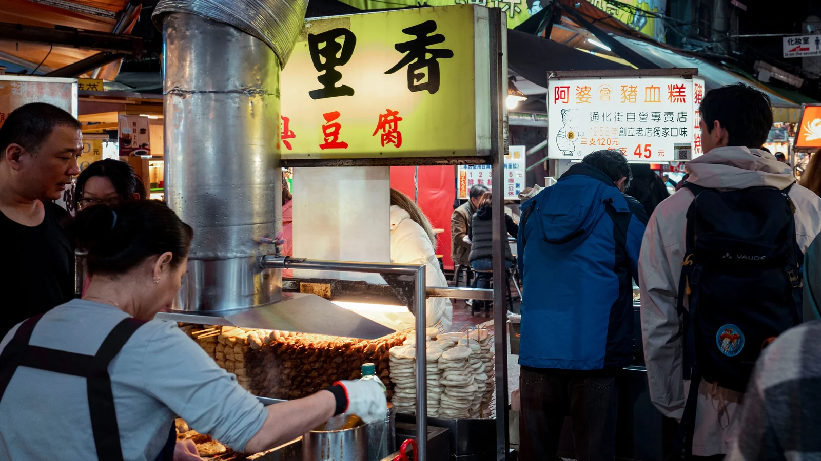 A lively Asian night market with open food stalls and travellers