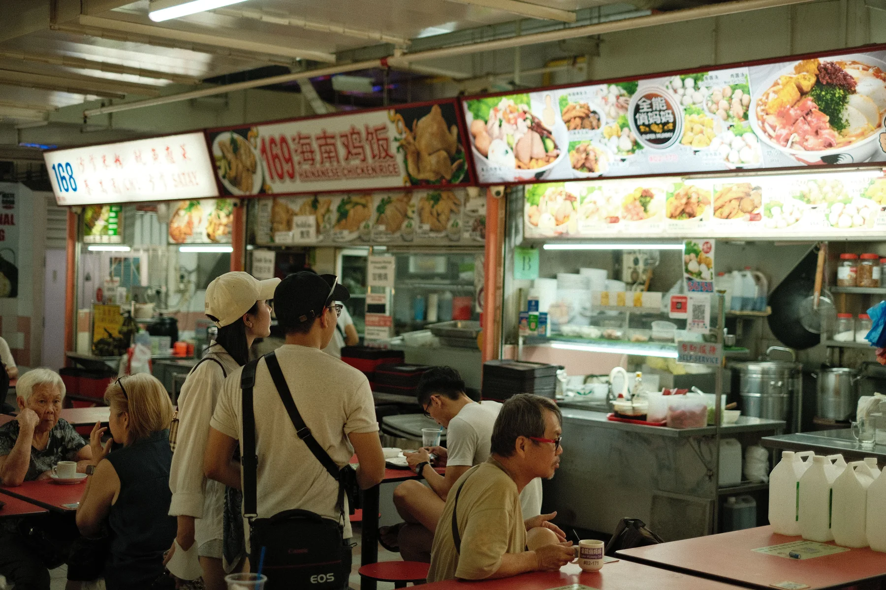 A busy Singapore hawker centre with multiple food stalls and shared tables