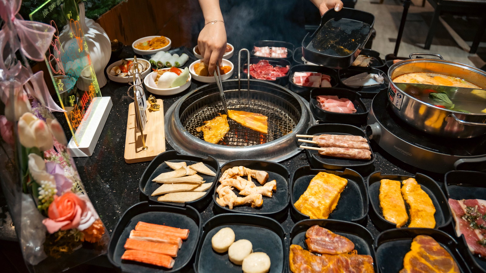 โต๊ะ Korean BBQ มีเตาย่างตรงกลาง เนื้อ ผัก และเครื่องเคียงหลายอย่าง