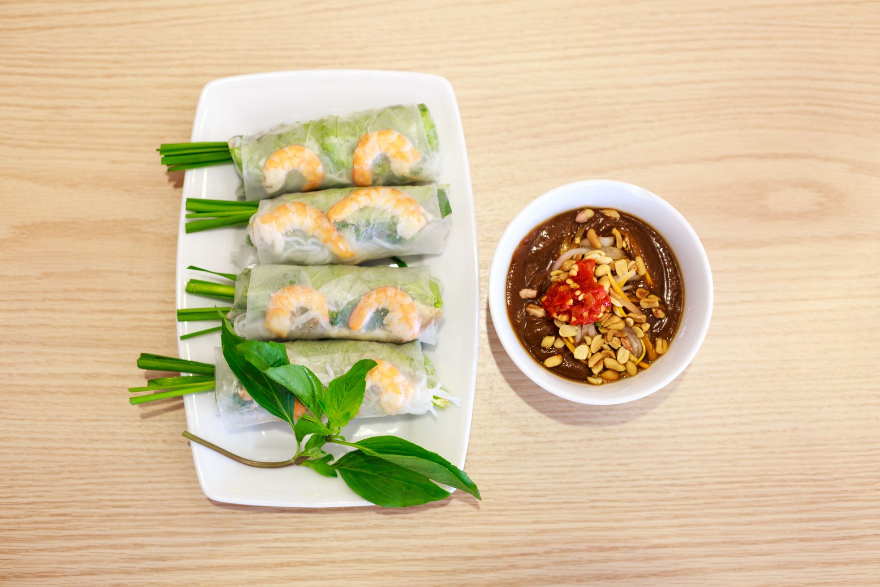 Vietnamese summer rolls with prawns, herbs and dipping sauce on a wooden table