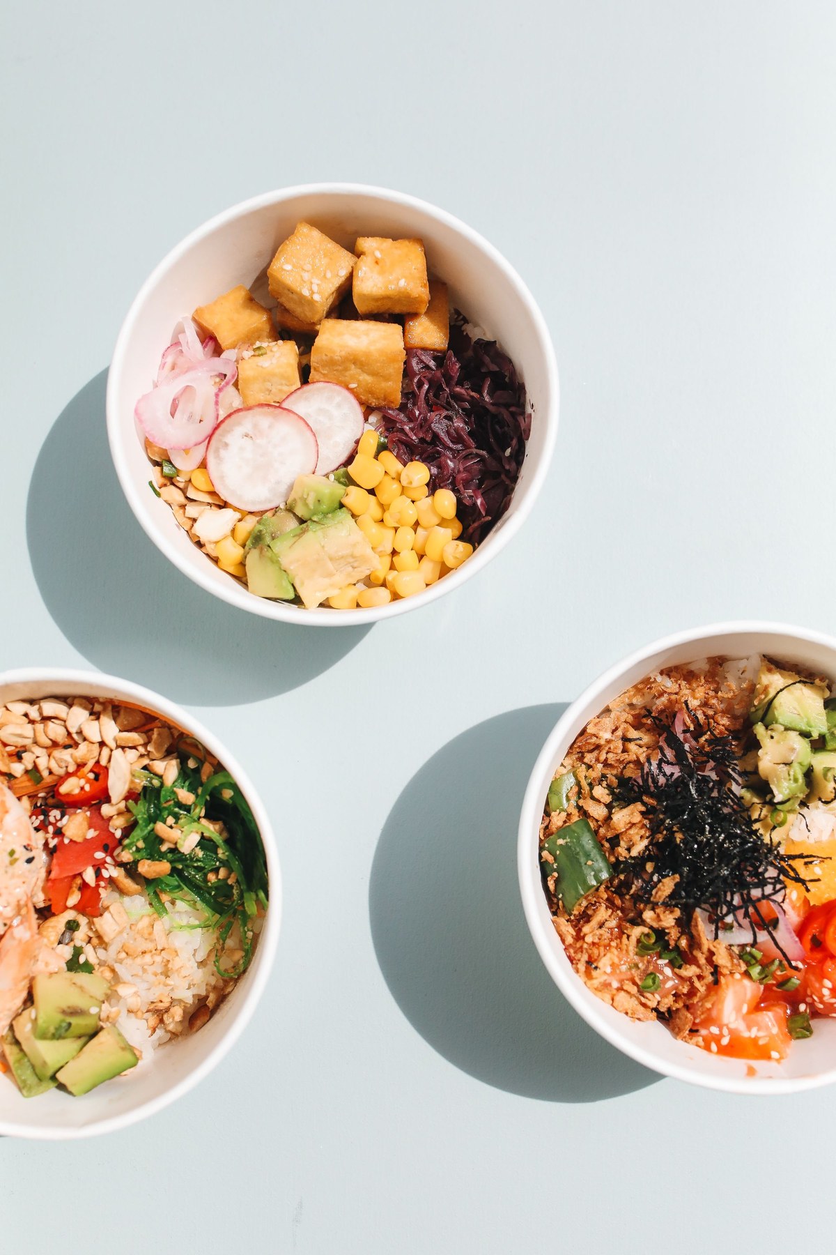 Several colourful poke bowls with rice, vegetables and different toppings
